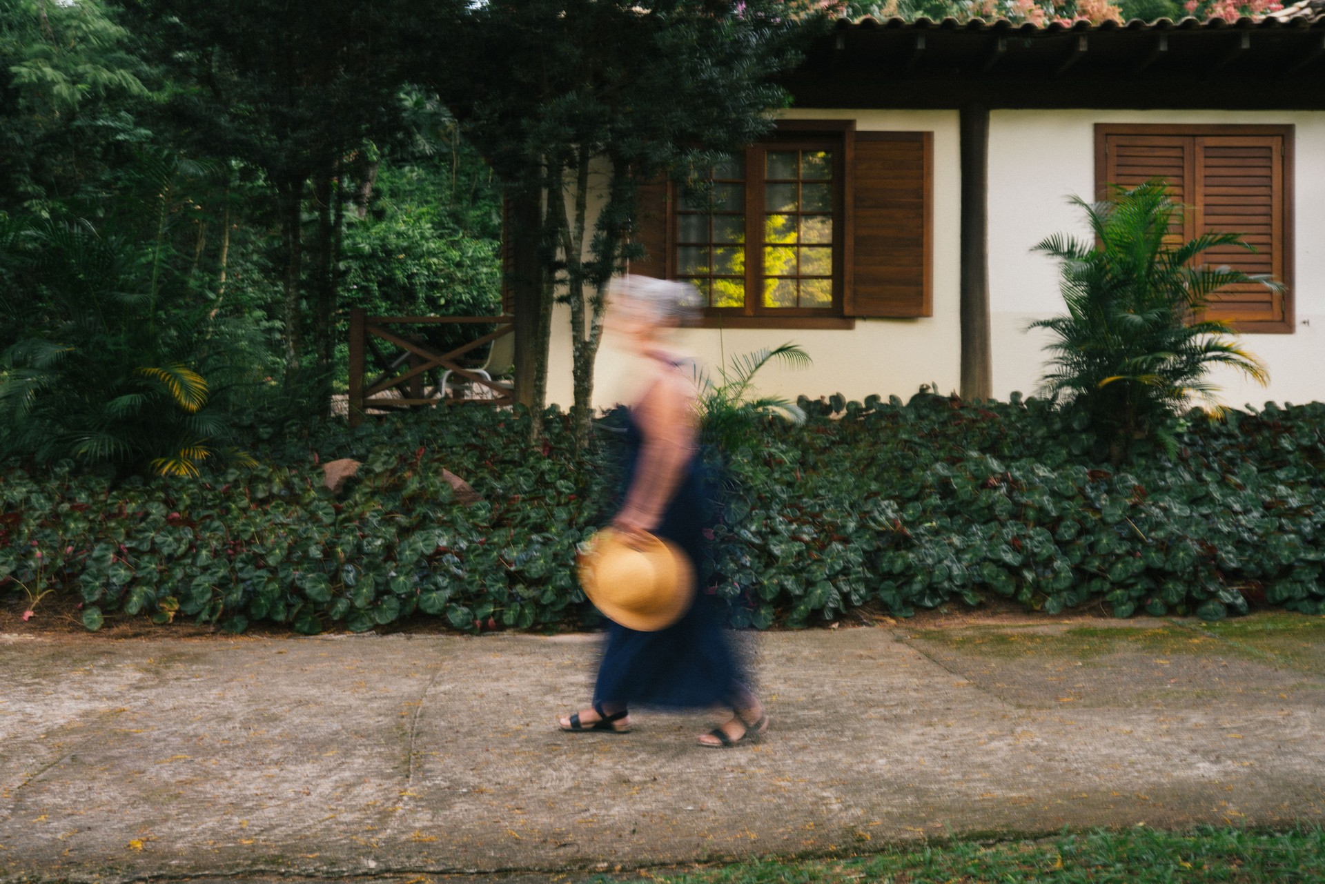 Imagem borrada de uma mulher andando na frente da casa, em um belo jardim